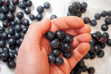 Fresh juicy blue berry in a hand in focus. Blue berry on a white surface out of focus.