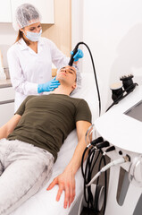 Obraz premium Woman cosmetologist giving facial electroporation procedure to male