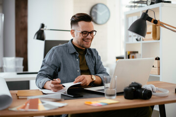Young businessman using laptop in his office. Businessman working and taking notes.
