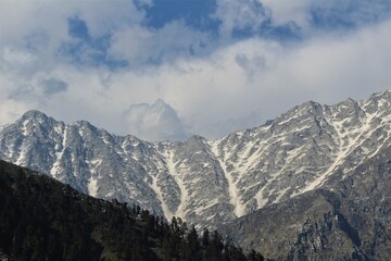 View of the majestic high altitude mountain ranges of the Himalayas with clouds on top them in broad daylight.