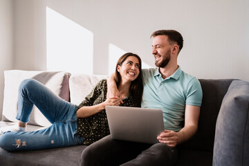 Smiling couple relaxing on the sofa with a notebook hugging each other