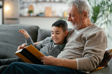 Grandfather and grandson reading a book. Grandpa and grandson enjoying at home.	
