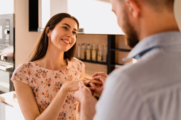 Woman smiling, happy while her man Putting On Engagement Ring To Her Finger On A Romantic Date at home