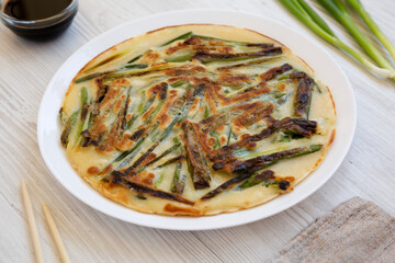 Homemade korean Pajeon scallion pancake on a white plate on a white wooden background, side view. Asian food. Close-up.