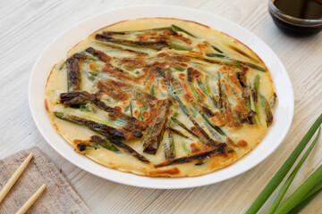 Homemade korean Pajeon scallion pancake on a white plate on a white wooden background, low angle view. Asian food. Close-up.
