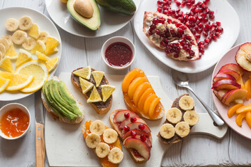 Process of making sweet toast with jam and various fruits apricots, peaches, bananas, oranges and avocado decorated with pomegranates on top.