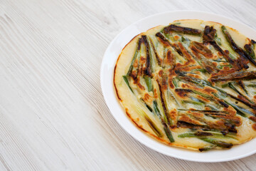 Homemade korean Pajeon scallion pancake on a white plate on a white wooden surface, side view. Asian food. Copy space.