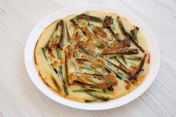 Homemade korean Pajeon scallion pancake on a white plate on a white wooden table, side view. Asian food. Close-up.