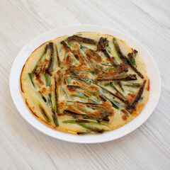 Homemade korean Pajeon scallion pancake on a white plate on a white wooden surface, side view. Asian food. Close-up.