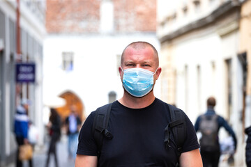 Portrait of brunette man in a medical surgical mask in the city.