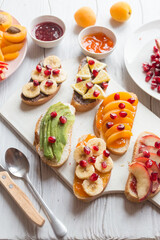 Sweet toast with jam and various fruits apricots, peaches, bananas, oranges and avocado decorated with pomegranates on top.