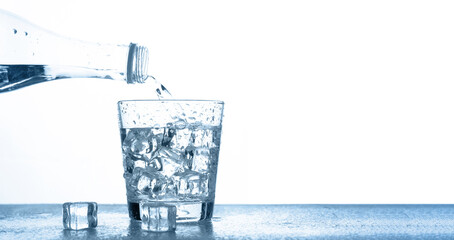 Pour drinking water into a clear glass with ice on the table on a white background with copy space.