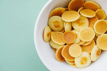 Freshly cooked pancake cereal in a bowl on mint green background.