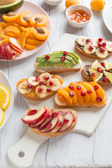 Sweet toast with jam and various fruits apricots, peaches, bananas, oranges and avocado decorated with pomegranates on top.
