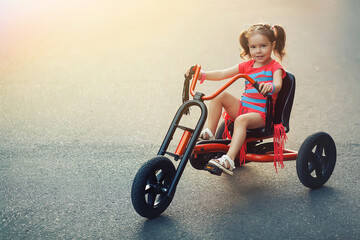 A four year old girl rides a red tricycle. she's riding on the tarmac. 