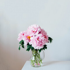 Beautiful bouquet of fresh pink peony flowers in full bloom in vase against white wall background.