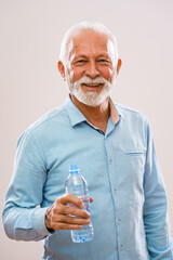 Portrait of cheerful senior man who is holding bottle of water and smiling.