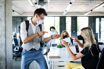 Young people with face masks back at work in office after lockdown, having fun.