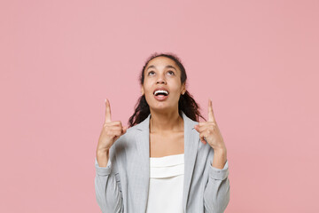 Excited young african american business woman in grey suit white shirt posing isolated on pink wall background studio portrait. Achievement career wealth business concept. Pointing index fingers up.