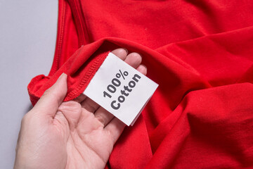 Hand holding red knit fabric clothes with 100% cotton label, tag, mark