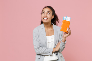 Pensive young african american business woman in grey suit white shirt posing isolated on pink background. Achievement career wealth business concept. Hold passport tickets boarding pass, looking up.