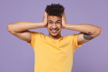 Displeased tired young african american guy in casual yellow t-shirt posing isolated on pastel violet wall background. People lifestyle concept. Mock up copy space. Put hands on head, having headache.