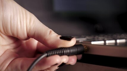 This close-up shot shows a girl plugging in a 3.5mm headphone jack into the audio input of her laptop before recording a new podcast.. High quality 4k footage