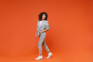 Fototapeta na wymiar Side view of cheerful young african american woman girl in gray casual clothes posing isolated on orange wall background studio portrait. People lifestyle concept. Mock up copy space. Looking aside.