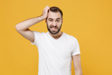 Preoccupied young bearded man guy in white casual t-shirt posing isolated on yellow wall background studio portrait. People sincere emotions lifestyle concept. Mock up copy space. Put hand on head.