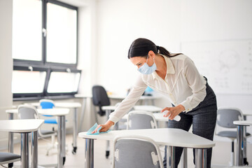 Teacher back at school after covid-19 quarantine and lockdown, disinfecting desks.