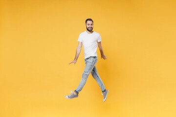 Fototapeta na wymiar Smiling young bearded man guy in white casual t-shirt posing isolated on yellow background studio portrait. People emotions lifestyle concept. Mock up copy space. Jumping spreading hands and legs.