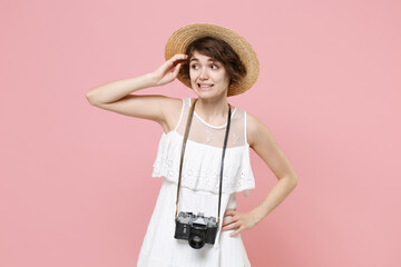 Preoccupied young tourist woman in summer dress hat with photo camera isolated on pink background....