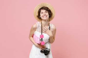 Smiling young tourist girl in dress hat with photo camera isolated on pink background. Traveling abroad to travel weekend getaway. Air flight journey concept. Hold skateboard, keeping eyes closed.
