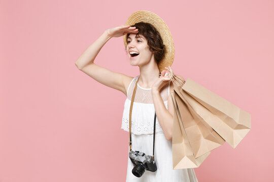 Tourist girl in dress hat with photo camera isolated on pink background. Traveling abroad to travel weekend getaway. Air flight journey concept. Hold package bag with purchases looking far away aside.