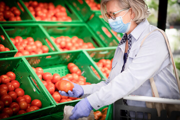 Senior woman wearing mask and rubber gloves shopping and choosing vegetables in supermarket, healthy eating active retired elderly people