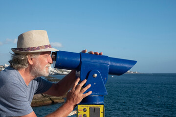 Side view of a senior man with beard and white hair using a binoscope. Horizon over the sea.  Sunny day. Happy and positive relaxed moment.