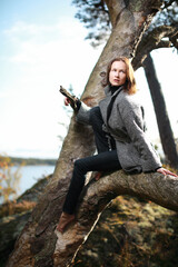 Beautiful caucasian woman in gray coat siting on the tree in the forest in autumn season 