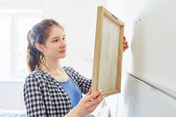 Junge Frau hängt ein Bild an der Wand auf
