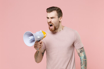 Irritated young bearded tattooed man guy in pastel casual t-shirt posing isolated on pink background studio portrait. People lifestyle concept. Mock up copy space. Scream in megaphone, looking aside.
