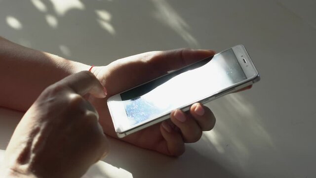 close up woman hand holding wite telephone smart phone screen golden sun light sunshine background sunny day internet searching application store notification weblink online video call