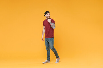 Fototapeta na wymiar Cheerful young tattooed man guy in casual t-shirt black cap posing isolated on yellow background studio portrait. People sincere emotions lifestyle concept. Mock up copy space. Pointing thumb aside.