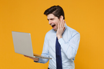 Irritated business man in classic blue shirt tie isolated on yellow background. Achievement career wealth business concept. Mock up copy space. Work on laptop pc computer screaming put hand on cheek.