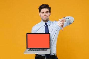 Dissatisfied young business man in classic blue shirt tie isolated on yellow background. Achievement career wealth business concept. Hold laptop pc computer with blank empty screen showing thumb down.