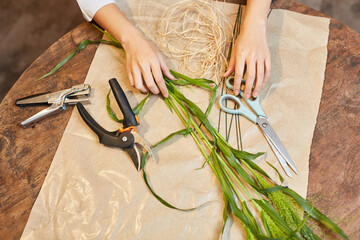 Hands of florist with flower scissors and bast