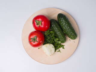 Tomatoes, cucumbers, onions and herbs on the board. Cooking for a salad. Vegetable ingredients