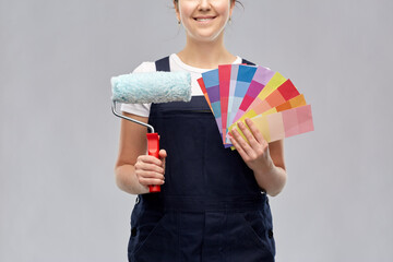 repair, construction and building concept - close up of happy smiling female painter or builder with paint roller and color charts over grey background