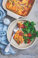 Classical baked frittata or omelet with tomatoes, peppers and cheese in white plate, light gray...