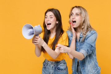 Two shocked young women girls friends in casual t-shirts denim clothes isolated on yellow...