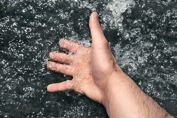 A man dips his hand in a stream of creek.
