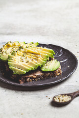 Avocado toast with rye bread and hemp seeds on black plate. Healthy vegan food concept.